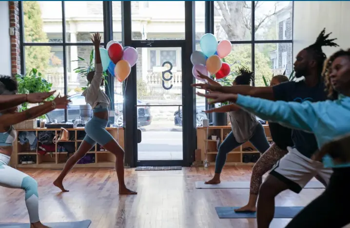 People practicing yoga indoors with colorful balloons near the entrance.