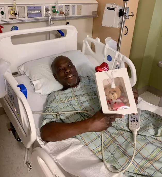 Elderly man smiling in hospital bed holding a photo frame.