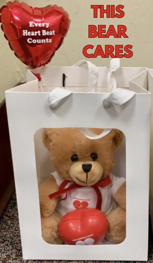 Teddy bear with a red bow inside a white gift bag.